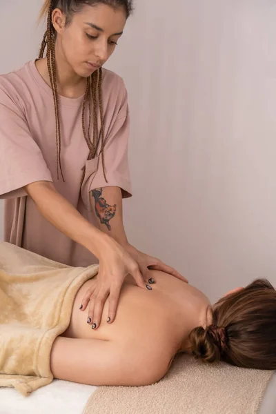 Female masseur massages the back and shoulder blades of a young brown-haired woman in a spa with soft lighting, close-up.Concept of body care, health, massage spa treatments.Vertically photo