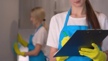 Tablet kontrollü genç bir temizlikçi. Grup Kuru Temizleme Şirketi çalışanları üniformalı, kız elinde kalemle tablet cihazı tutuyor, yüksek kaliteli hizmet. Önlüklü profesyonel silecekler. Üniforma.