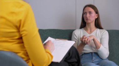 Kadın psikolog konuşur ve kıza yardım eder. Önemli çalışmaları tablete kaydediyor, arkadan ya da arkadan görüyor. Psikoloji, akıl sağlığı kavramı. Dikey video. Psikoterapistle görüşme.