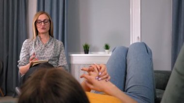 Kadın psikolog konuşur ve kıza yardım eder. Önemli çalışmaları tablete kaydediyor, arkadan ya da arkadan görüyor. Psikoloji, akıl sağlığı kavramı. Dikey video. Psikoterapistle görüşme.