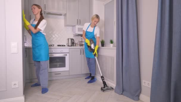 現代のロフトアパートで働く制服清掃員の専門チーム 女性は垂直真空クリーナーとワイプキッチンで床をきれいにします 現代のアパートのクリーニング会社の広告 — ストック動画