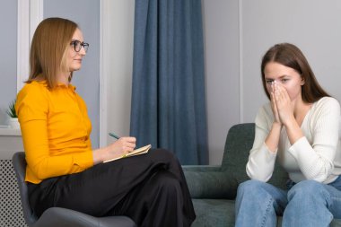 Genç üzgün kadın bir psikoterapist randevusunda ellerini yüzüne dayayıp kanepede oturuyor. Psikolog ve bir müvekkili seansta. Psikolojik sağlık ve kişisel bakım kavramı.