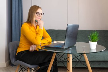 Portakal rengi bluz ve gözlüklü genç bir kadın psikolog cam bir masada oturuyor ve bir psikoloji merkezinde online danışmanlık yapıyor..