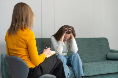 Psikolog randevusundaki genç bir kadın kanepede oturuyor ve kafasını tutuyor, negatif duygular yaşıyor. Psikoloji, psikosomatik kavramı