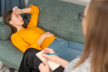 Genç bir kadın, kadın bir psikologla terapi görüyor. Kanepede uzanıyor ve durum hakkında çok endişeli. Bir psikologla seans..