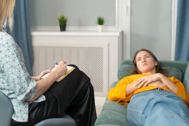 Genç bir kadın yanında bir psikologla kanepede uzanıp dinleniyor ve psikolojik terapi sırasında ona destek oluyor. Bir psikoterapistle seans sırasında rahatlama. Psikosomatik..