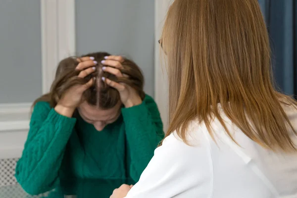 Young woman sitting at a table at a psychologist\'s appointment, feeling hopeless and depressed, with her head in her hands. Focus on the psychologist