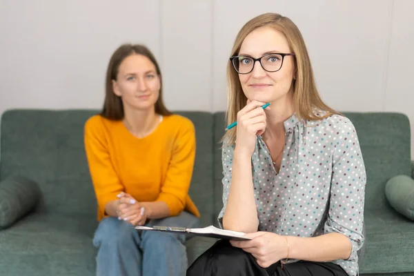 戴眼镜笑着的女心理学家看着摄像机 向办公室里一个微笑的年轻女人咨询 心理问题 心理支持和专业帮助 — 图库照片