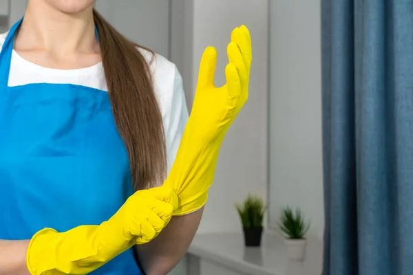 Close-up of a professional maid putting on rubber gloves before cleaning, cleaning service company. Concept of housekeeping, cleaning