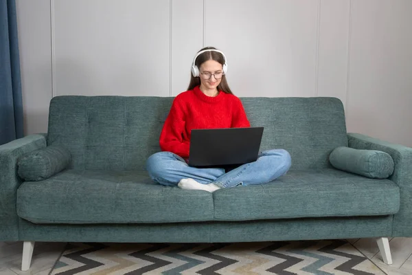스웨터에 청바지에 헤드폰을 소파에서 인터넷 서핑을 사무실에서 일하는 프리랜서는 노트북 — 스톡 사진