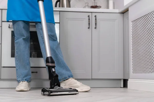 Modern bir mutfağı temizlerken elinde elektrikli süpürge tutan bir kadının yakın çekimi. Temizlik şirketinin çalışanı ya da ev hanımı evi temizler..