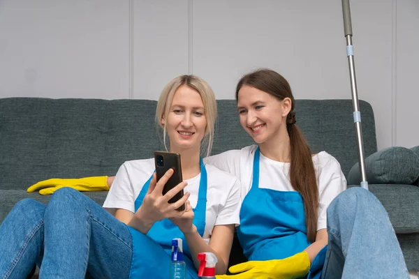 전문가 아파트에서 앞치마를 가정용 청소용 생산물 스마트폰 화면을 보면서 웃는다 — 스톡 사진