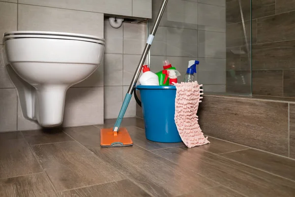 Blue bucket with cleaning products, a rag, a mop are on the floor in a beautiful modern bathroom. Concept of cleaning, restoring order in the house