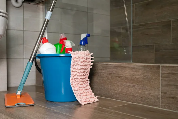 Close up blue bucket with cleaning products, a rag, a mop are on the floor in a beautiful modern bathroom. Concept of cleaning, restoring order in the house