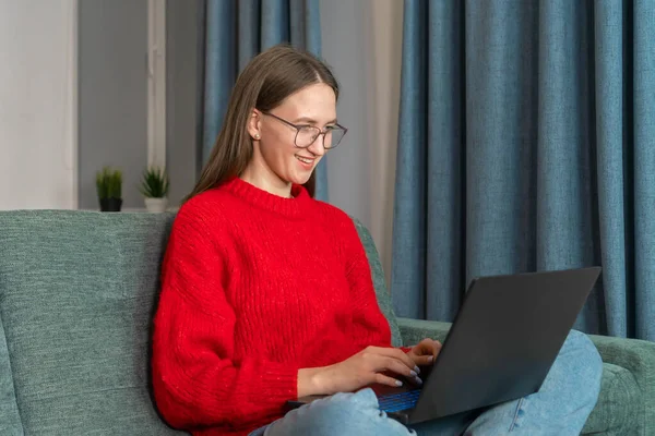 스웨터에 청바지 안경을 노트북을 소파에 행복하게 있습니다 아름다운 소녀가 하거나 — 스톡 사진