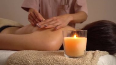 Masör spa salonunda kadın vücuduna masaj yapıyor. Güzellik tedavisi konsepti. Aroma mumu ön planda iki atmosfer sıcaklığı ve rahatlıkla yanar. Vücut bakımı, güzellik ve sağlık.