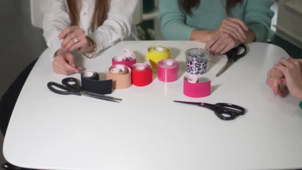 Bőrfelvarrás Kinesziotapizálás Lányok Asztalhoz Ülnek Ollóval Vágják Fel Színes Kineziotázs — Stock videók