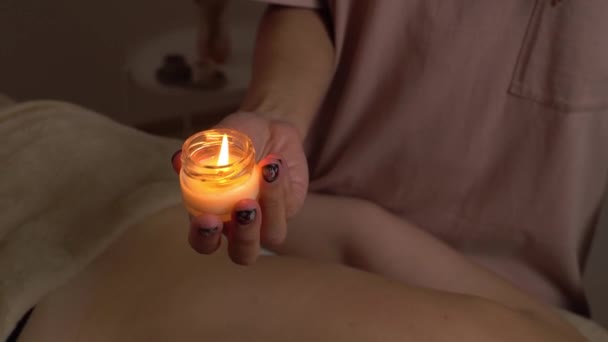 女性のマッサージ師の手はワックスを溶融し ホットマッサージを作るために彼女の手に熱い香りキャンドルを保持しています スパでアロマセラピー 皮膚や健康管理 リラックス — ストック動画