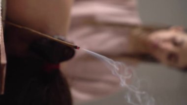 Kadın masör, yanan çubuğun arka planında hasta masajı yapıyor dumanlı, aromaterapili. Spa odası, masaj masası, havlular, kozmetik ürünleri, masaj yağları, tütsü çubukları. Dikey video