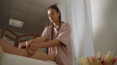 Beyaz kadın güzellik salonunda ayak ve ayak masajı yapıyor, yüz manzaralı. Masör, genç ve güzel bir kızın ayağını ve bacağını mumların arka planına karşı yoğurdu..