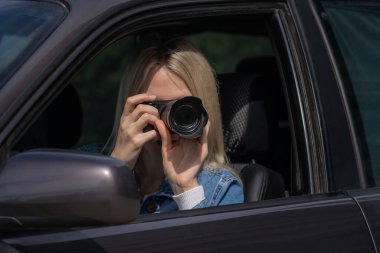 Genç sarışın kadın arabada otururken fotoğraf çekiyor. Gazetecilik kavramı, dedektif, papparation