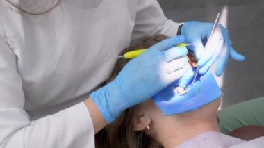 Dişe reçine bazlı bileşik dolgu uygulanıyor. Dişçi kliniğindeki genç kadın. Modern diş muayenehanesinde dişçi ve asistanı hastaların ağız boşluklarını tedavi ediyor..