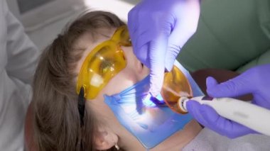 Diş hekimi hastanın dişini dolgu malzemesiyle doldurur ve asistanı güzel bir kadına ultraviyole lamba tutar. Diş yenileme ameliyatı. Diş dolgusu için UV.