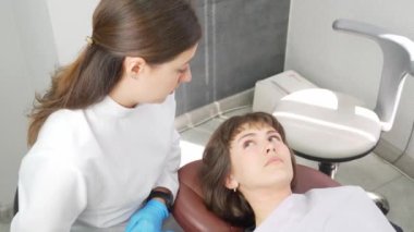 Mutlu genç Avrupalı kadın dişçiyle tatlı tatlı iletişim kuruyor ve diş kliniğinde resepsiyon sırasında konuşuyor. Modern tıp. Kadın gülümsüyor ve doktora diş sorunlarını anlatıyor..