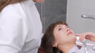 Mutlu genç Avrupalı kadın dişçiyle tatlı tatlı iletişim kuruyor ve diş kliniğinde resepsiyon sırasında konuşuyor. Modern tıp. Kadın gülümsüyor ve doktora diş sorunlarını anlatıyor..