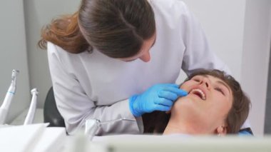 Modern ofisteki dişçi aletin yardımıyla güzel kız hastada diş muayenesi yapıyor. Sağlıklı beyaz zumları olan bir kadın sandalyeye oturur. Diş hekimliğinde profesyonel iş..