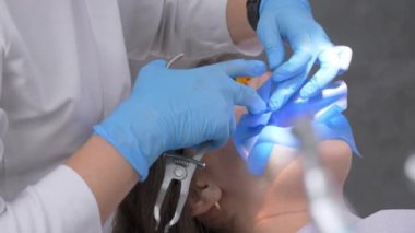 Diş hekimi lateks atkıyı kanalların ve pulpitlerin tedavisi için metal klipslerle hazırlıyor. Lateks yalıtımlı kumaş ağız boşluğuna monte edilir. Çürük dişlerin tedavisi ve restorasyonu