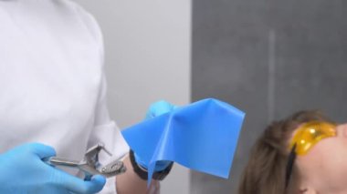 Diş hekimi lateks atkıyı kanalların ve pulpitlerin tedavisi için metal klipslerle hazırlıyor. Kerpeten latekste delik açıyor. Kumaş yalıtımı ve çürük dişlerin restorasyonu.
