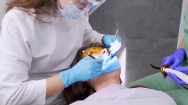 Dişçi kadın klinikte genç bayan hastaların dişlerini tedavi ediyor. Diş hekimi diş matkabı ve diş cilası kullanırken yüz maskesi takar. Modern dişçi muayenehanesinde dişçi prosedürleri. Lateks peçete. lastik.