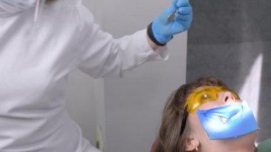 Kadın dişçi ve asistan diş kalkülüsünü dişlerinden çıkarıyor. Ziyaret, profosyonel diş kliniğinde. Kadın dişçi koltuğunda oturuyor. Diş delme ve işleme, dolgu.