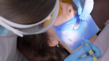 Dişçi kadın klinikte genç bayan hastaların dişlerini tedavi ediyor. Asistan mührü kurutmak için ultraviyole mor ötesi lamba getiriyor. Modern dişçi muayenehanesinde dişçi prosedürleri. Lateks peçete. lastik.