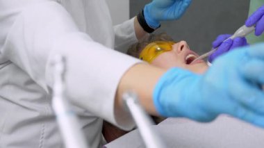 Dişçi kadın klinikte genç bayan hastaların dişlerini tedavi ediyor. Diş hekimi diş matkabı ve diş cilası kullanırken yüz maskesi takar. Modern dişçi muayenehanesinde dişçi prosedürleri. Lateks peçete. lastik.