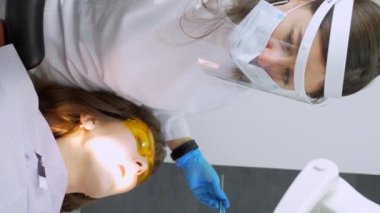 Dişçi kadın klinikte genç bayan hastaların dişlerini tedavi ediyor. Diş hekimi diş matkabı ve diş cilası kullanırken yüz maskesi takar. Modern dişçi muayenehanesinde dişçi prosedürleri. Lateks peçete. lastik.