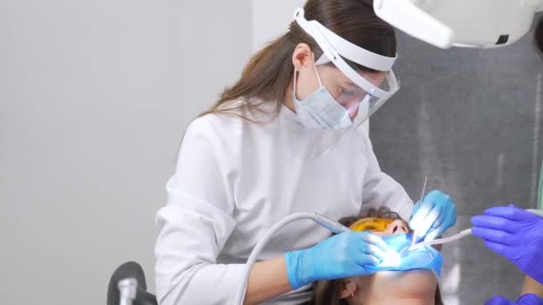 歯医者と助手は歯から歯の微積分を除去する 訪問は専門の歯科クリニックにあります 女性は歯の椅子に座っている 歯の掘削と治療 — ストック動画