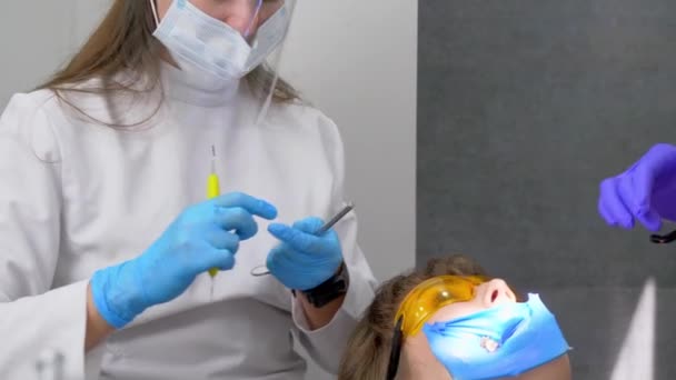 充填および重合ランプで歯の復元 歯科クリニックでの紫外線硬化で歯科充填乾燥手順中の若い女の子 助手の業務 — ストック動画