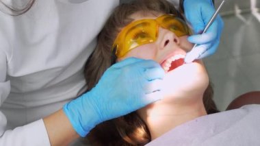 Modern ofisteki dişçi aletin yardımıyla güzel kız hastada diş muayenesi yapıyor. Sağlıklı beyaz zumları olan bir kadın sandalyeye oturur. Diş hekimliğinde profesyonel iş..