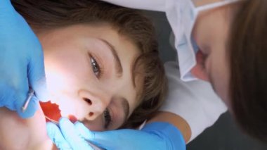 Modern ofisteki dişçi aletin yardımıyla güzel kız hastada diş muayenesi yapıyor. Sağlıklı beyaz zumları olan bir kadın sandalyeye oturur. Diş hekimliğinde profesyonel bir iş. dikey video