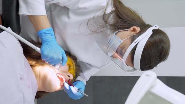 歯医者の女性は診療所で若い女性患者の歯を治療する 歯科医は 歯科用ドリルと研磨歯を使用する際にフェイスマスクを着用します 現代の歯医者の診察室で ラックス ナプキン — ストック動画