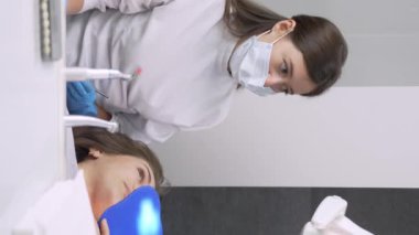Mutlu genç Avrupalı kadın dişçiyle tatlı tatlı iletişim kuruyor ve diş kliniğinde resepsiyon sırasında konuşuyor. Modern tıp. Kadın gülümser ve doktora diş sorunlarını anlatır. dikey video