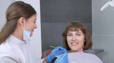 Dişçi koltuğundaki gülümseyen kız doktoruna özgüvenle bakar ve sonra gözlerini kameraya çevirir ve gülümser, yakın plan. Modern klinikte profesyonel dişçi tarafından diş tedavisi