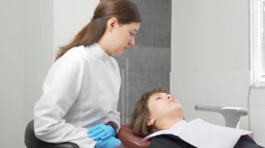 Mutlu genç Avrupalı kadın dişçiyle tatlı tatlı iletişim kuruyor ve diş kliniğinde resepsiyon sırasında konuşuyor. Modern tıp. Kadın gülümsüyor ve doktora diş sorunlarını anlatıyor..