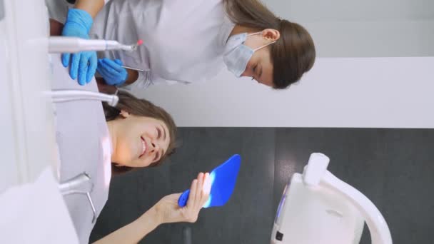 快乐的年轻欧洲女性与牙医甜蜜地交流 并在预约期间在牙科诊所对着镜子与自己交谈 现代医学 女人笑着告诉医生问题 — 图库视频影像