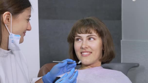 歯科医の椅子の笑顔の女の子は自信を持って彼女の医者を見て その後 カメラと笑顔 クローズアップに彼女の視線を向ける 現代のクリニックの専門歯科医による歯科治療 — ストック動画