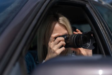 Genç sarışın kadın arabada otururken fotoğraf çekiyor. Gazetecilik kavramı, dedektif, papparation