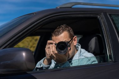 Dedektif Pivate ve güneş gözlüklü, arabada oturuyor ve gözetleme yapıyor, profesyonel bir kamerayla fotoğraf çekiyor.