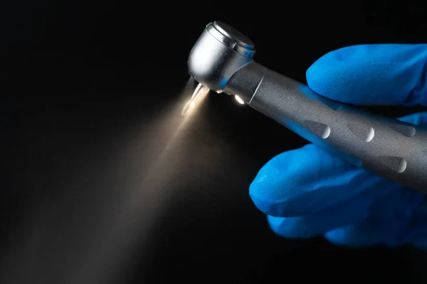 Dentist hand with drill illustrates operation of dentist dental drill machine with water. Dentist\'s hands with blue gloves working with dental drill in dental office. Close up, selective focus